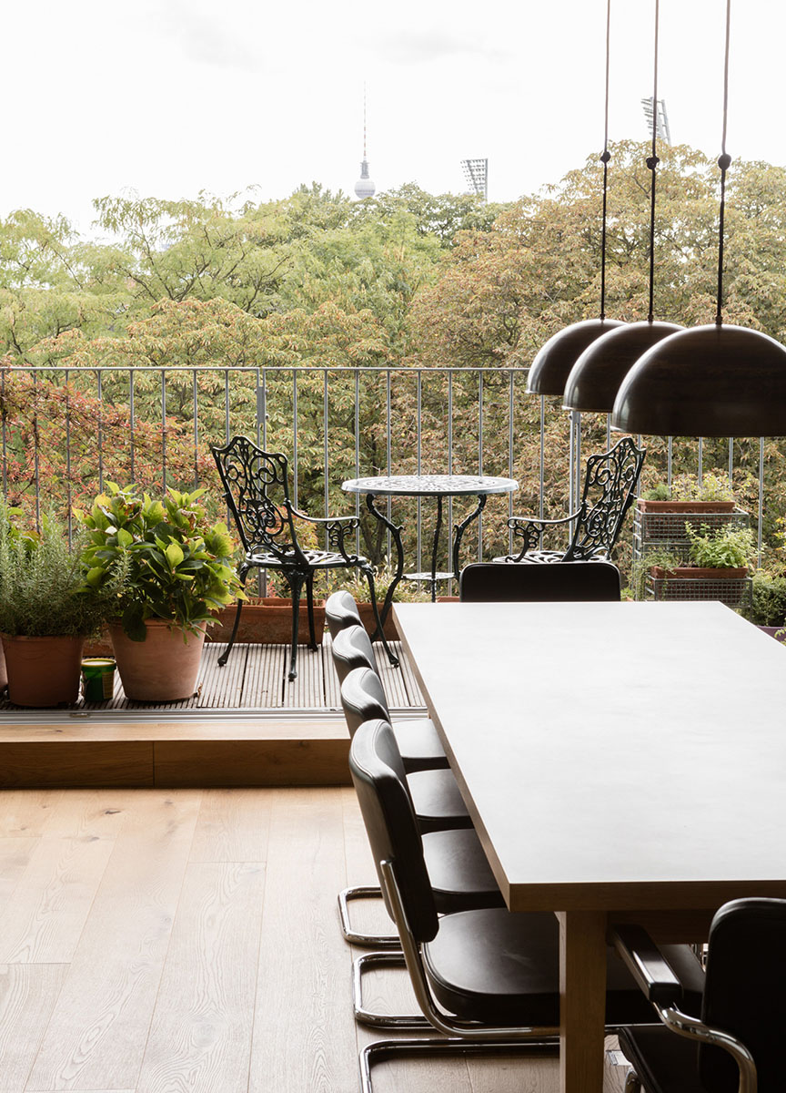 Block an einem langen Esstisch vorbei auf einen Balkon mit Ausblick über Baumkronen